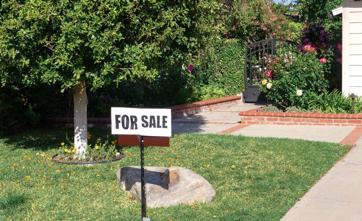 A For Sale sign in the front yard of a suburban home