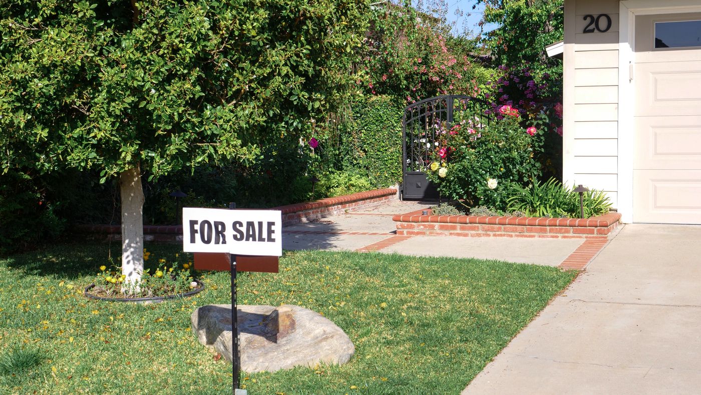 A For Sale sign in the front yard of a suburban home